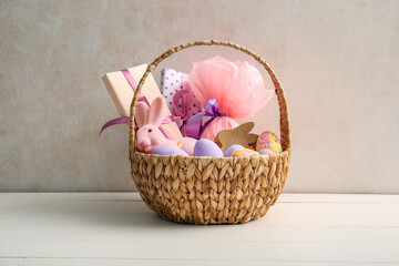 Fototapeta na wymiar Wicker basket with painted Easter eggs, toy bunny and gift boxes on white wooden table