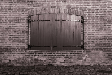 Zamknięta drewniana okiennica w ceglanej ścianie w czerni i bieli
