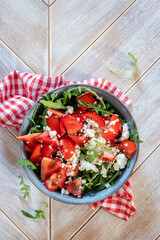 Healthy vegetable salad with fresh arugula, tomato, feta cheese and walnut on dark plate. Diet menu. Top view. Salad with arugula