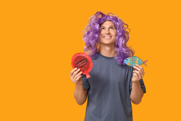 Handsome young man in funny disguise with whoopee cushion and paper fish on yellow background....