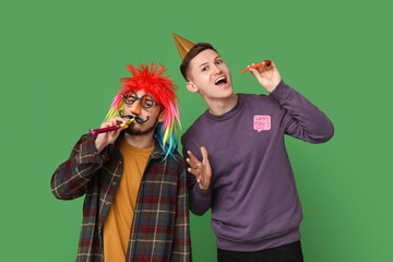 Young friends in funny disguise with party whistles and sticker on green background. April fool's...