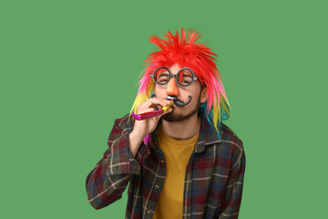 Handsome young man in funny disguise with party whistle on green background. April fool's day...