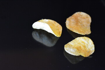 Food, product, potato pieces, potato chips arranged on black glossy background.