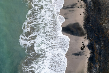 White waves crashing on a sandy seashore. Top view, drone photo