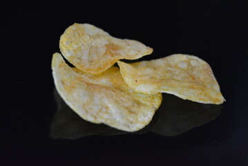 Food, product, potato pieces, potato chips arranged on black glossy background.
