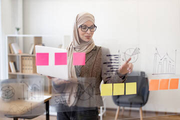 Confident muslim woman in formal wear and hijab solving business issues with laptop in hands while standing at company boardroom. Concept of modern technology and busy people.