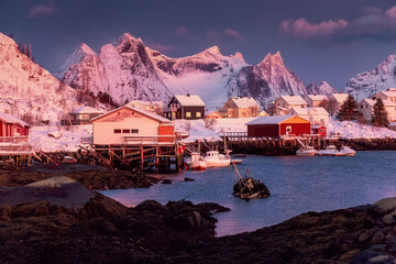 Norwegian fishing village with red rorbu houses, mountain peaks and sea coast winter sunset...