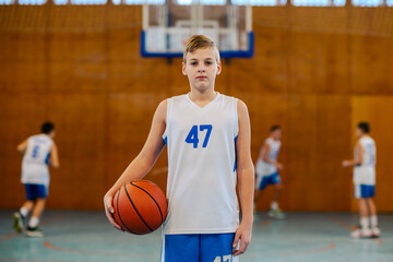 Fototapeta premium A young basketball player posing on court with a ball.