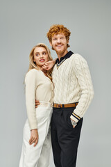 cheerful man and blonde woman in trendy casual attire standing and posing on grey, old money style