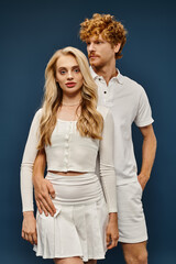 attractive blonde woman in white clothes looking at camera near redhead aristocratic man on blue