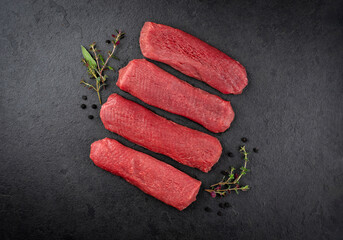 Raw lamb salmon fillet offered as top view on a rustic black board with dried cranberries and herbs with copy space © HLPhoto