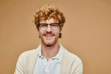 portrait of cheerful redhead man in eyeglasses and trendy light-colored clothes on beige backdrop