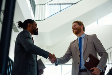 Below view of happy businessmen handshaking in hallway.