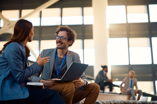 Happy businessman talking to female colleague while using laptop in convention center.