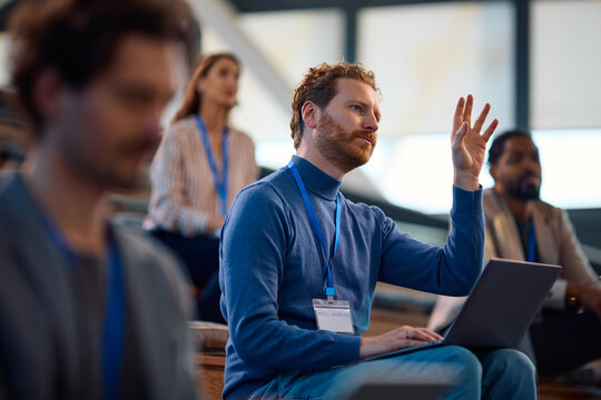 Male entrepreneur raising his hand to ask question while attending business seminar in conference room.