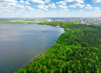 Fototapeta na wymiar Big lake with green shores in bright sun light and city on horizon, aerial landscape. Recreation concept. Aerial view