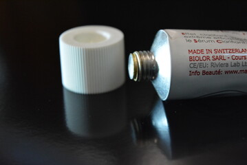 Cosmetics, white anti-inflammation cream in a white metal tube placed on a black glossy background.