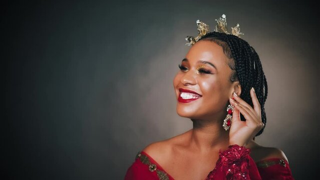 fantasy portrait happy african american woman princess beauty smiling face. Girl queen golden crown on head hand puts on touches earring. Red dress fairy lady carnival costume. black dark gray studio