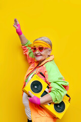 funny granny in hipster clothes listening to music on a tape recorder and showing a kiss on a...