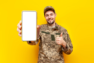 Ukrainian army soldier in military camouflage uniform shows smartphone screen and like on yellow...
