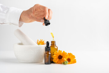Calendula flowers in mortar, amber glass bottles with essential oil and pharmacist hand with...