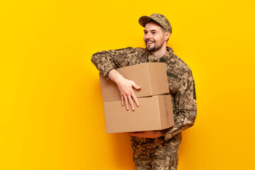 Ukrainian army soldier in pixel camouflage uniform holds box on yellow isolated background,...