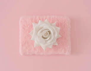 White colored rose on pastel pink and faux fur background. Minimal aesthetic layout. Romantic creative idea. Spring and summer fashion concept with blooming flower. Flat lay.