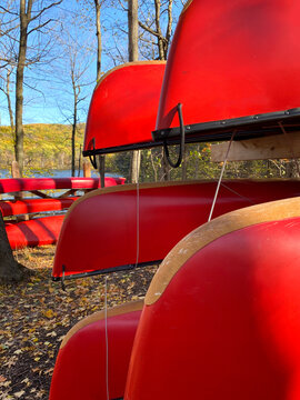 Red canoes on wooden supports. Forest in autumn. Nautical boat rental, river canoe, rabaska in a national park. Outdoor center for camping and fishing.