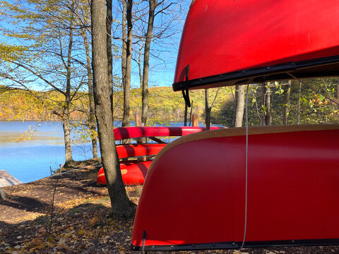 Red canoes on wooden supports. Forest in autumn. Nautical boat rental, river canoe, rabaska in a national park. Outdoor center for camping and fishing.