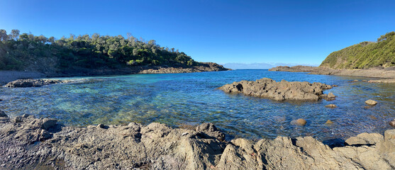 Panoramic view of a rocky coast of the sea. Turquoise ocean water, mountains, shore and rocks in a bay. Coastal landscape.