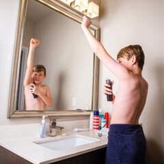 Preteen boy standing at bathroom mirror spraying deodorant under his arm © 3Days2Go Media