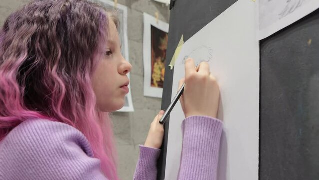Cute girl with pink hair painting on canvas, holding pencil, enjoying creative hobby, childhood, training artistic skills.