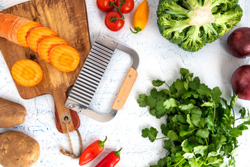 wavy knife for curly slicing vegetables. Carrot slices on a cutting board. Onions, broccoli, tomatoes and parsley top view.