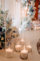 Large white voluminous candles stand on the floor at a wedding ceremony in blue evening light. Warm candlelight. Warm light, cold shadows. Shiny glass. Candles are lit in elegant glass vases on the fl