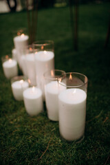 Large white voluminous candles stand on the floor at a wedding ceremony in blue evening light. Warm candlelight. Warm light, cold shadows. Shiny glass. Candles are lit in elegant glass vases on the fl