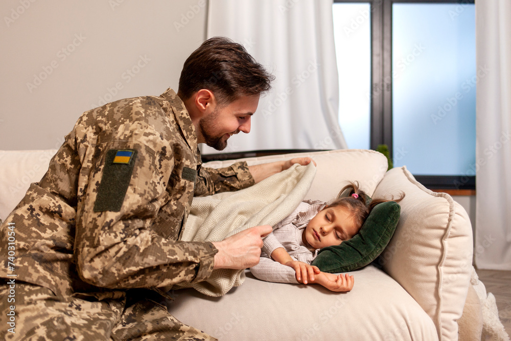 Canvas Prints happy soldier of Ukrainian army in camouflage uniform returned home and puts his daughter to bed, military dad protects and takes care of child at home, concept of mobilization in Ukraine