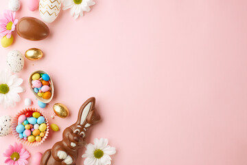 Сhocolate bunnies meet spring blossoms. Top view shot of chocolate Easter bunnies, assorted Easter eggs, and white flowers on pastel pink background with space for promotions or Easter greetings