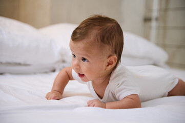 Close-up portrait of lovely baby boy in white bodysuit during tummy time. Kids development stage and baby growth concept