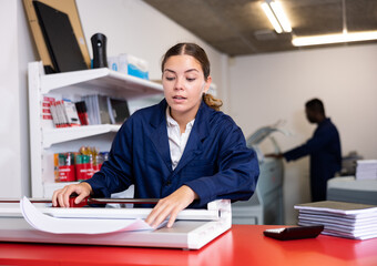 Work in printing house - woman cuts paper with a professional cutter