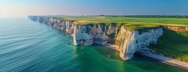 Sunlit white cliffs stand out against emerald sea, green fields above and clear sky