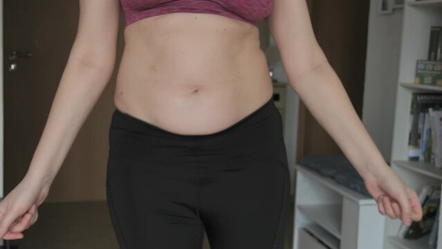 Female belly body positive. Woman dancing belly dance in flat slow motion. Small layer of fat on abdomen of woman wearing a sports bra and leggings. Concept of sport, healthy lifestyle or overweight