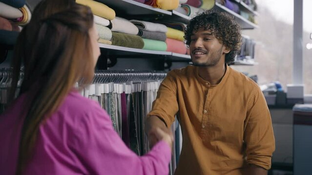 Female saleswoman seller fashion consultant talking with male customer in clothing store fabric shop happy Indian Arabian man Caucasian woman shake hands handshake successful deal purchase handshaking