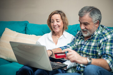 elderly couple with bank card and laptop on sofa