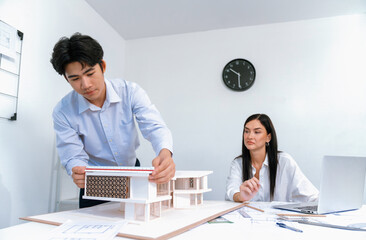 Professional male asian architect using ruler to measure house model length while young beautiful...