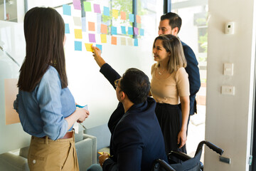 Team of businesspeople using sticky notes on a glass wall in a meeting room - obrazy, fototapety, plakaty