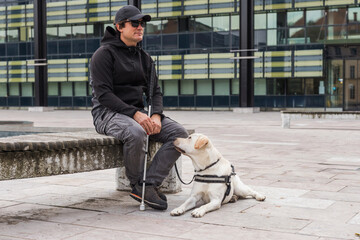 Blind man and his guide dog sitting on the street. Visually impaired people and assistance dogs...