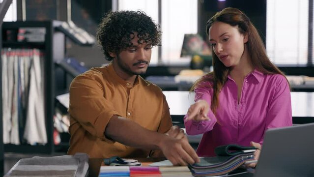 Female designer helping male client choose fabric material showing textile samples in office studio multiracial Arabian Indian man and Caucasian woman discuss color palette for interior house design