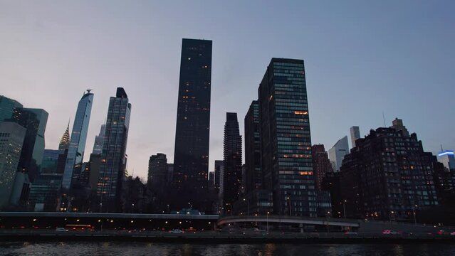 NYC New York City midtown east skyline pov point of view from river ferry, seeing many modern skyscrapers, upper Manhattan, office buildings, towers, and traffic during a blue hour night time ride