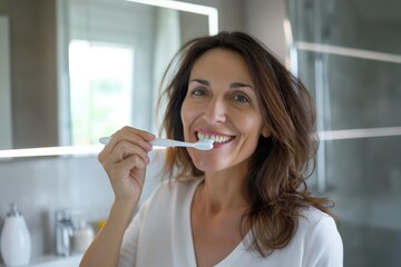Middle-aged woman happily brushes her teeth with a toothbrush in the bathroom.