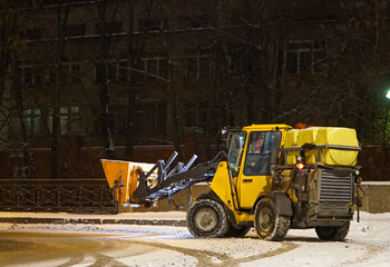 A snowplow cleans the sidewalks. A snowplow clears the street of snow at night. Selective focus....